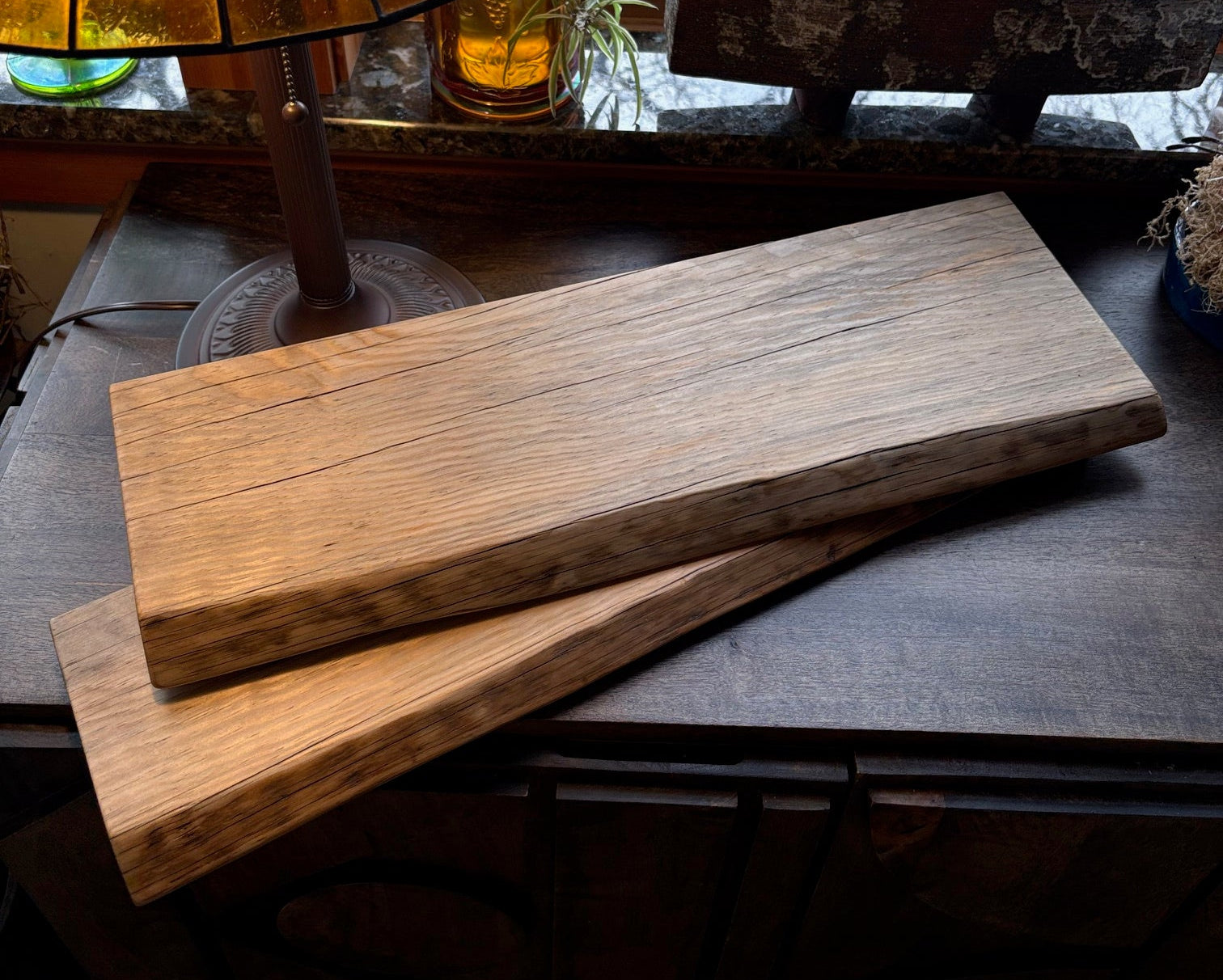 Two shelves made from warm-tone Ponderosa Pine wood, live edge facing the camera, both items situated beneath an incandescent lamp. The feeling of the image is cozy, like being in a warm cabin when it's raining outside. The image makes you want to buy the shelves.